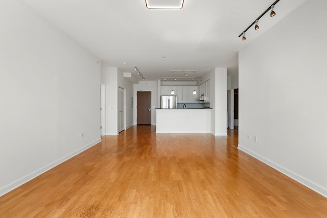 unfurnished living room featuring rail lighting, attic access, light wood-type flooring, and baseboards