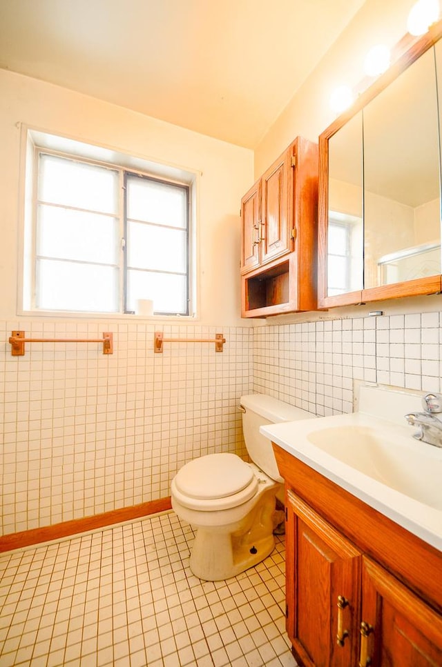 bathroom with tile walls, toilet, tile patterned flooring, vanity, and a wainscoted wall