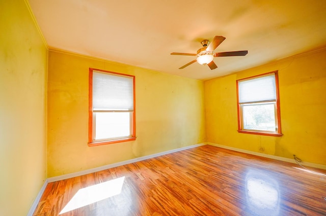 spare room with crown molding, baseboards, wood finished floors, and a ceiling fan