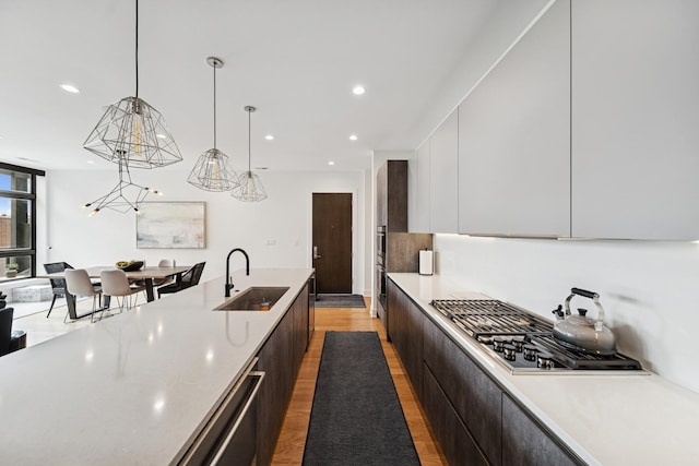 kitchen with a sink, pendant lighting, modern cabinets, light countertops, and light wood-style floors