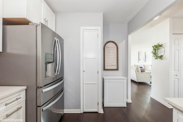 kitchen with stainless steel fridge, dark wood-style floors, light countertops, white cabinets, and baseboards