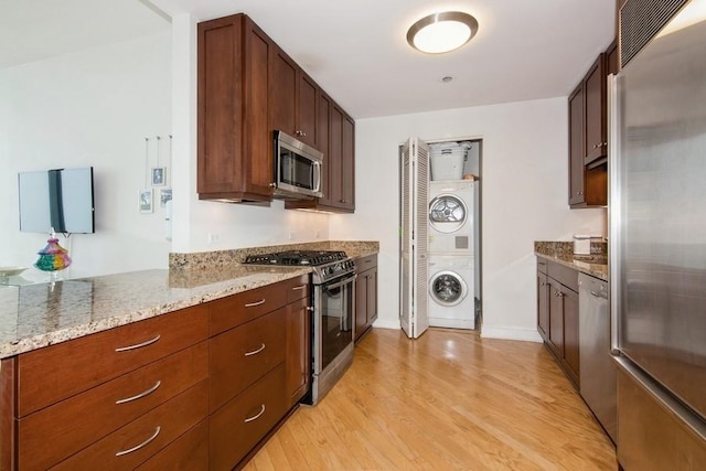 kitchen featuring stacked washer and dryer, stainless steel appliances, light wood-type flooring, baseboards, and light stone counters