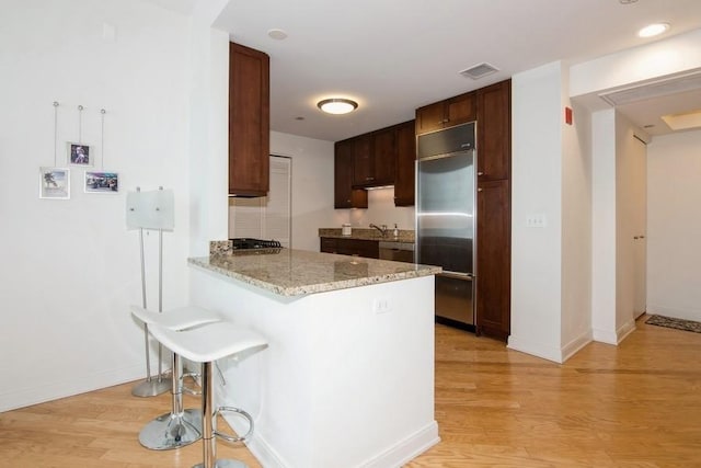 kitchen featuring a peninsula, stainless steel appliances, light wood-style flooring, and baseboards
