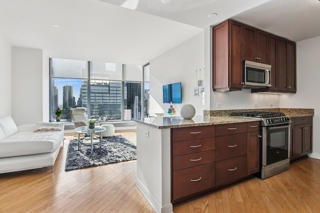 kitchen with stainless steel appliances, open floor plan, light stone countertops, dark brown cabinets, and light wood-style floors