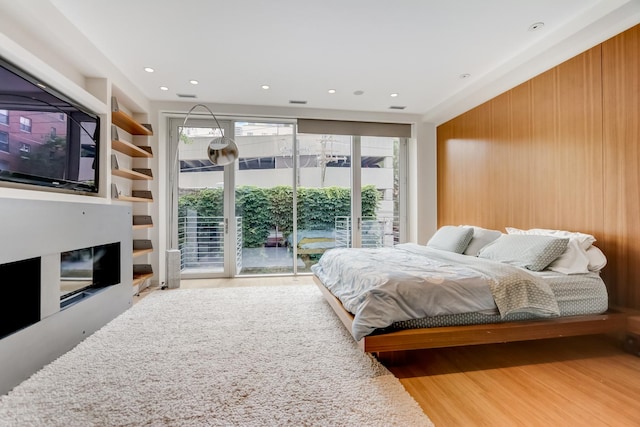 bedroom featuring wood finished floors, visible vents, wooden walls, a glass covered fireplace, and access to exterior