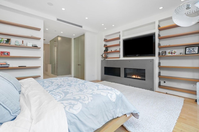 bedroom with recessed lighting, visible vents, wood finished floors, and a glass covered fireplace