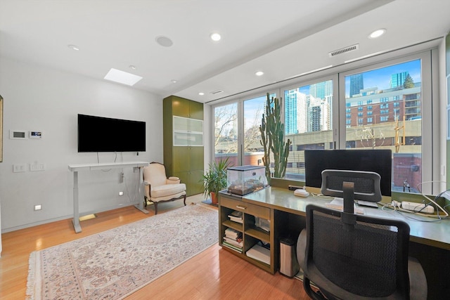 home office with light wood-style floors, visible vents, a skylight, and recessed lighting