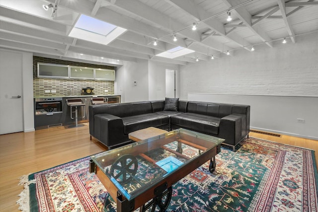 living room featuring beam ceiling, baseboards, track lighting, and light wood-style floors