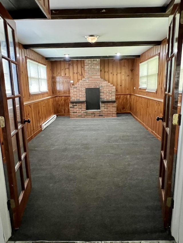 unfurnished living room featuring wooden walls, dark carpet, beam ceiling, and a baseboard heating unit