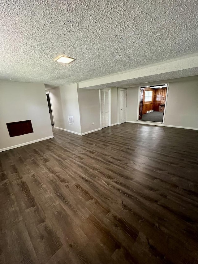 unfurnished living room featuring dark wood-type flooring, a textured ceiling, and baseboards