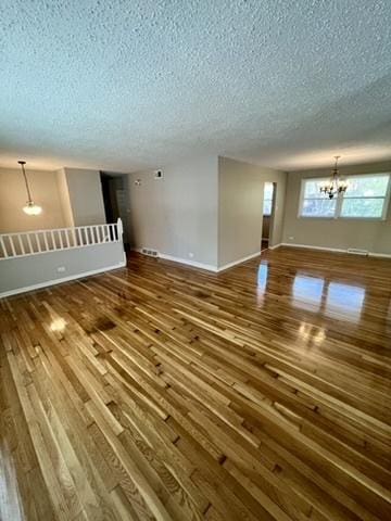 unfurnished living room with a chandelier, a textured ceiling, dark wood-style flooring, plenty of natural light, and baseboards
