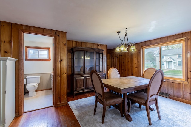 dining room with wood walls, a notable chandelier, baseboards, and wood finished floors