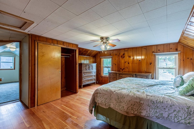 bedroom featuring multiple windows, wooden walls, and light wood-type flooring