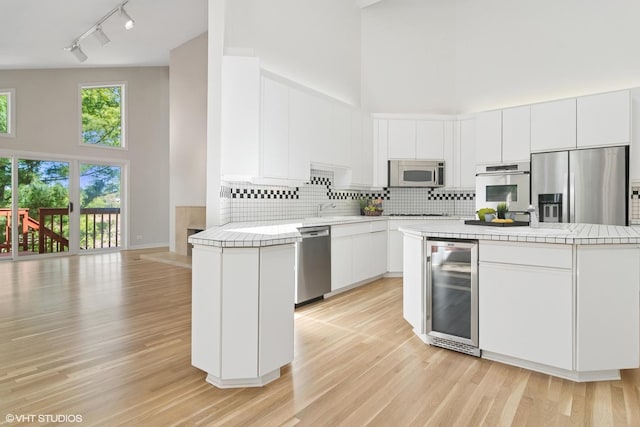 kitchen with beverage cooler, appliances with stainless steel finishes, a towering ceiling, track lighting, and tile counters