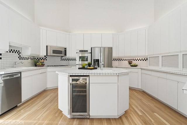 kitchen featuring beverage cooler, stainless steel appliances, tasteful backsplash, white cabinets, and a sink