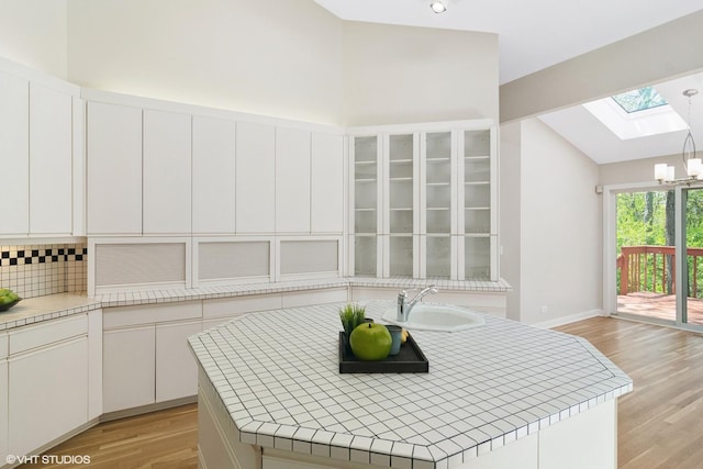 kitchen with a sink, a skylight, lofted ceiling, light wood-style flooring, and white cabinets