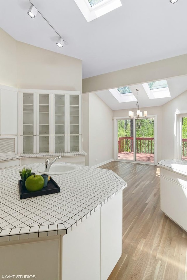kitchen featuring a skylight, tile countertops, track lighting, a chandelier, and light wood-style floors