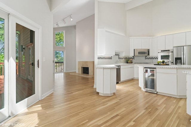 kitchen with stainless steel appliances, high vaulted ceiling, beverage cooler, track lighting, and decorative backsplash