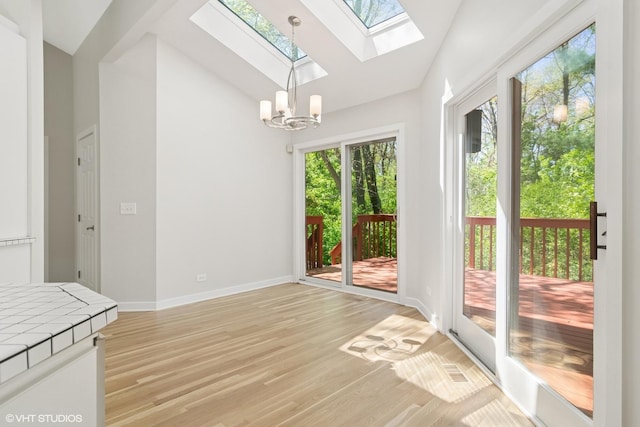 unfurnished dining area with lofted ceiling, a skylight, a chandelier, baseboards, and light wood-style floors