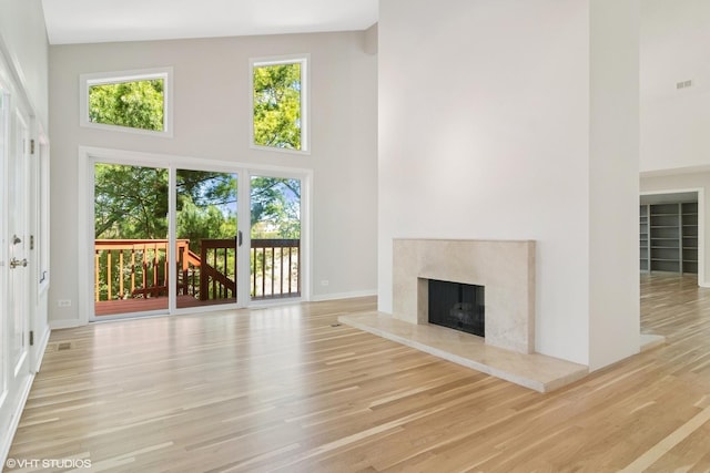 unfurnished living room featuring a high ceiling, a fireplace, wood finished floors, and baseboards