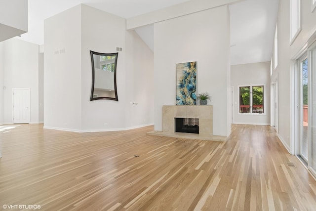 unfurnished living room with high vaulted ceiling, light wood-style flooring, baseboards, and a fireplace