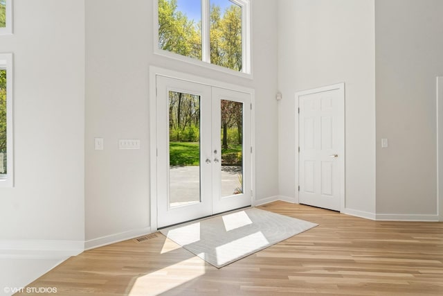 doorway to outside with french doors, a towering ceiling, light wood finished floors, and baseboards