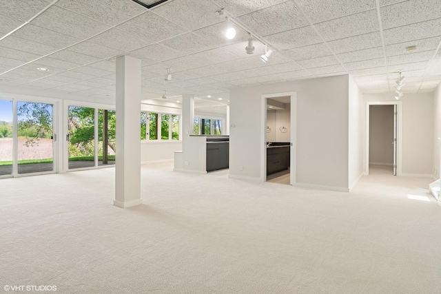 below grade area featuring rail lighting, light colored carpet, and baseboards