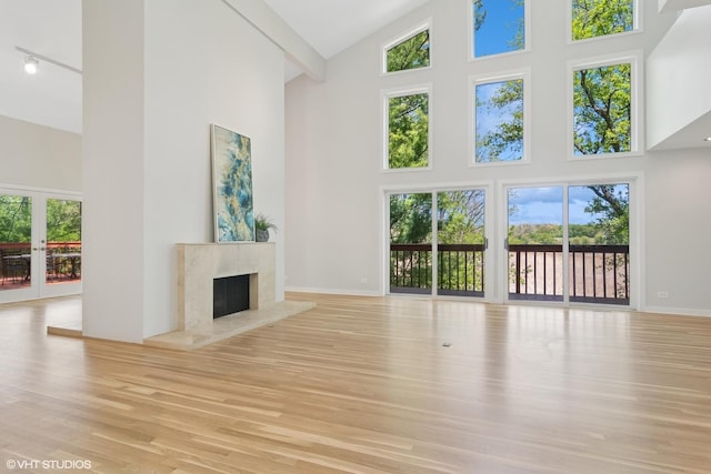 unfurnished living room with high vaulted ceiling, wood finished floors, a fireplace, baseboards, and french doors