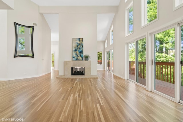 unfurnished living room with a towering ceiling, light wood-style floors, plenty of natural light, and baseboards