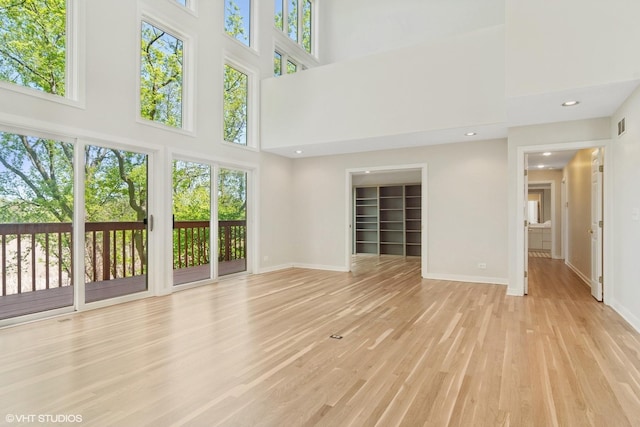 unfurnished living room featuring a towering ceiling, healthy amount of natural light, light wood-style flooring, and baseboards