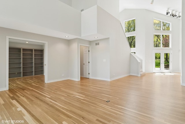 unfurnished living room featuring high vaulted ceiling, light wood-style floors, baseboards, built in shelves, and french doors