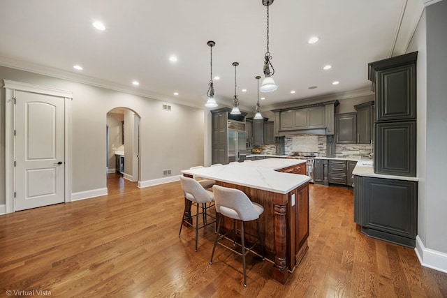 kitchen featuring a center island, high quality appliances, arched walkways, backsplash, and ornamental molding