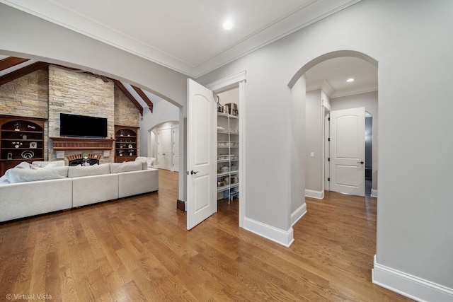 interior space with wood finished floors, ornamental molding, vaulted ceiling, arched walkways, and baseboards