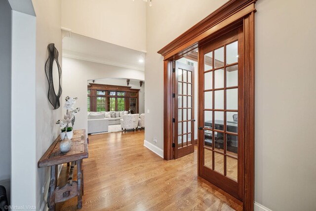 entryway featuring baseboards, light wood finished floors, french doors, and a high ceiling