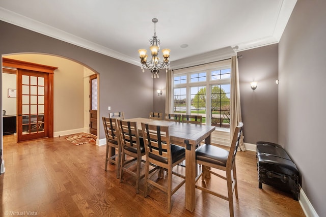 dining area featuring arched walkways, baseboards, crown molding, and wood finished floors