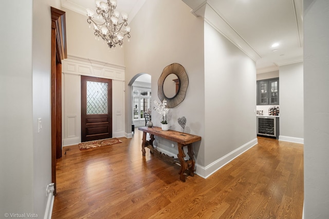 foyer entrance with a notable chandelier, beverage cooler, baseboards, ornamental molding, and arched walkways