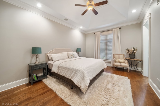 bedroom with a tray ceiling, wood finished floors, baseboards, and ornamental molding