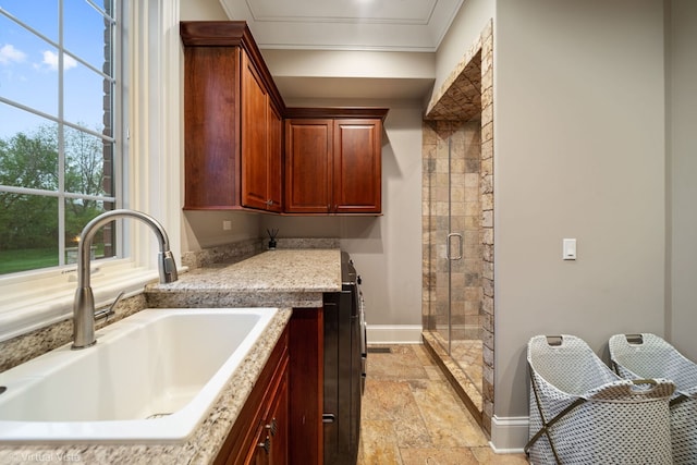 clothes washing area with baseboards, crown molding, a sink, and stone tile flooring