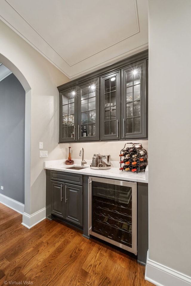 bar featuring a sink, indoor wet bar, wood finished floors, wine cooler, and arched walkways
