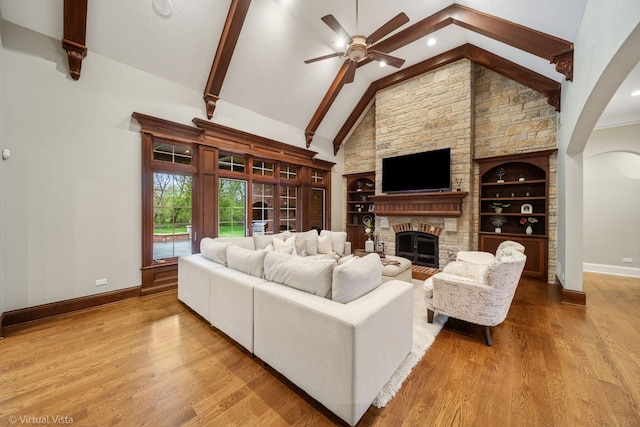 living room featuring baseboards, ceiling fan, wood finished floors, a fireplace, and vaulted ceiling with beams