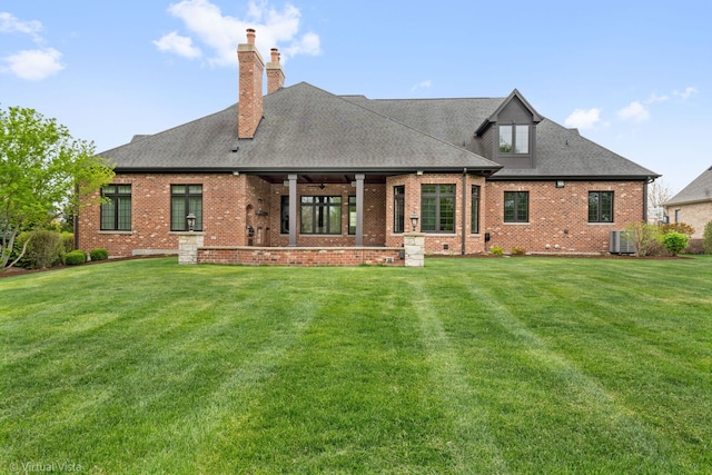 rear view of house featuring a yard, a chimney, brick siding, and central AC unit