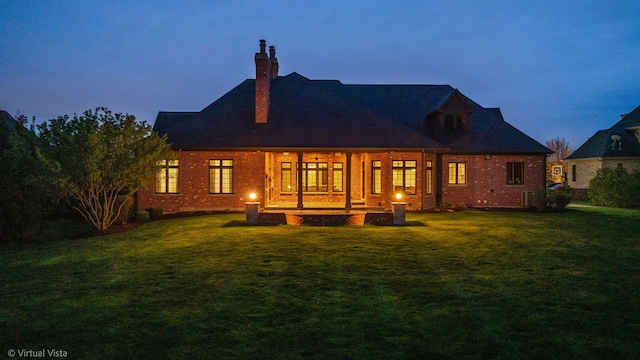 rear view of house featuring a yard, a chimney, and brick siding