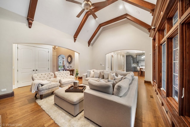 living room with light wood-style floors, a ceiling fan, arched walkways, and high vaulted ceiling