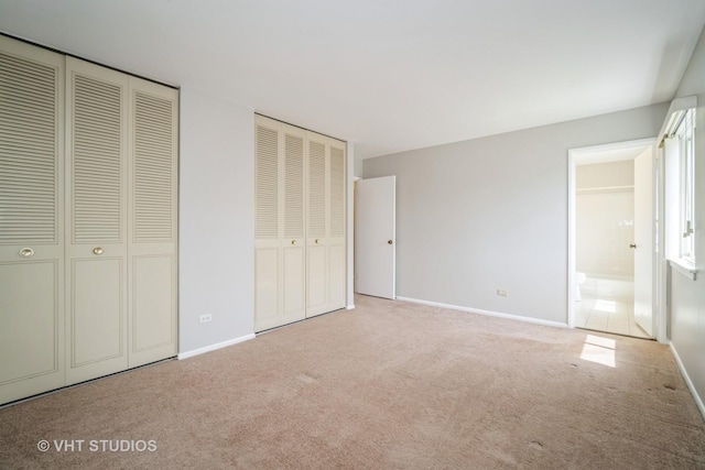 unfurnished bedroom with two closets, carpet floors, baseboards, and ensuite bathroom