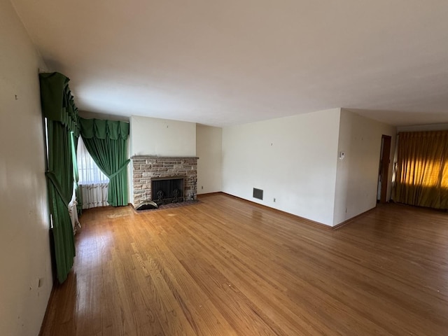 unfurnished living room featuring baseboards, a stone fireplace, visible vents, and wood finished floors