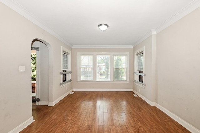 empty room with wood finished floors, baseboards, and ornamental molding