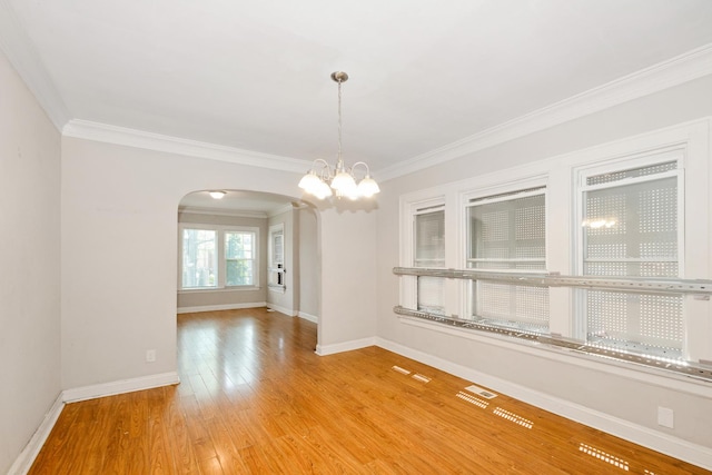 unfurnished dining area featuring arched walkways, wood finished floors, crown molding, baseboards, and a chandelier