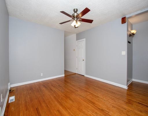 unfurnished room featuring a ceiling fan, a textured ceiling, baseboards, visible vents, and wood finished floors