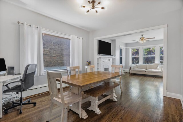 dining space with baseboards, a fireplace, dark wood-style floors, and ceiling fan with notable chandelier