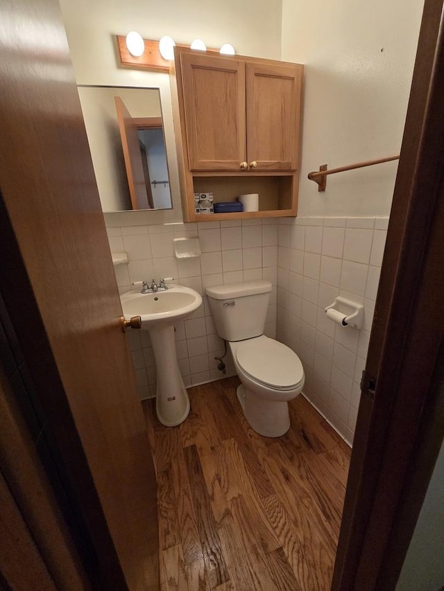 half bath featuring toilet, wood finished floors, a sink, a wainscoted wall, and tile walls